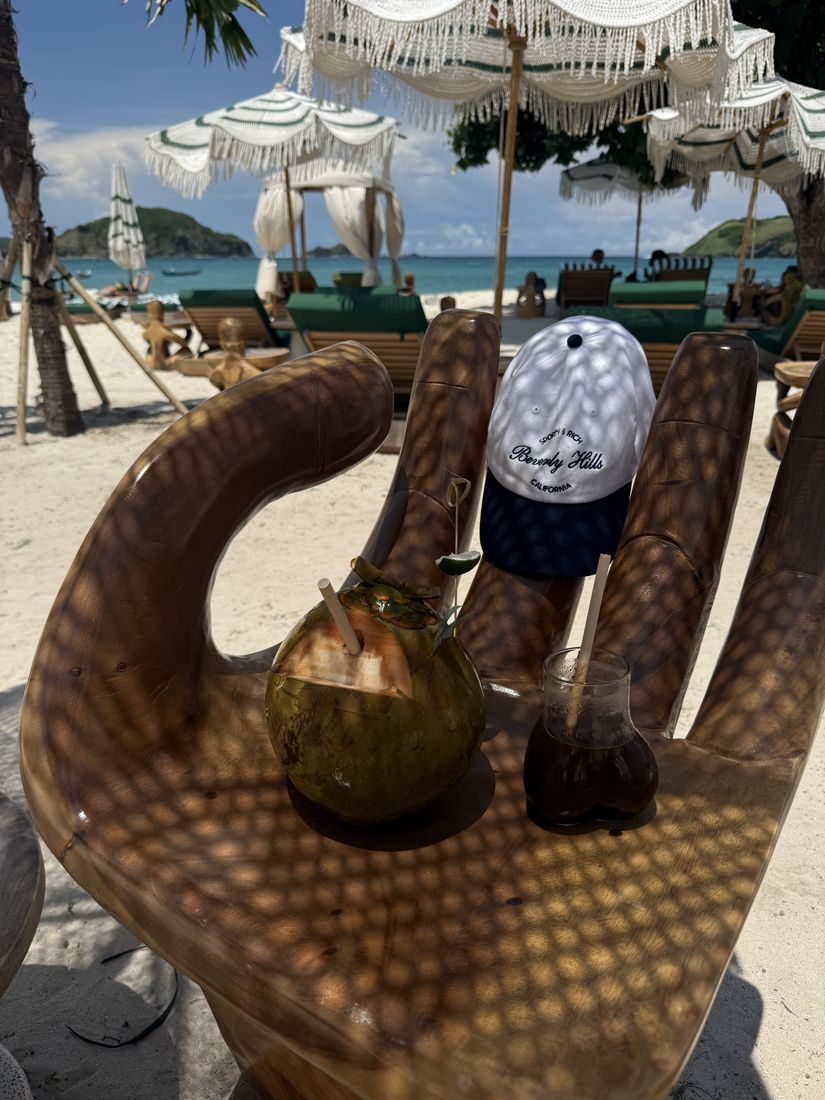 Kokosnøtt og drikke i en håndformet trestol på en strand med parasoller